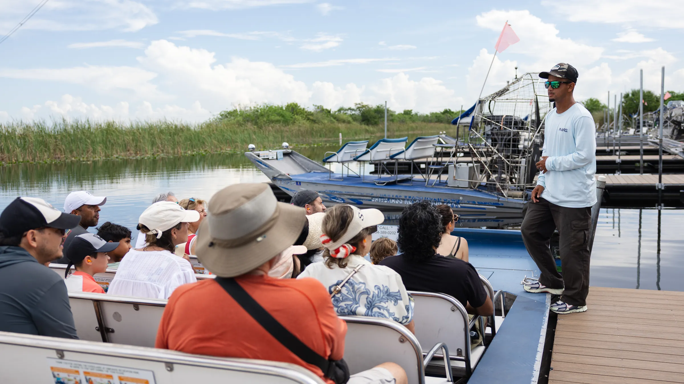 Group on a boat listening to a guide near water and reeds.