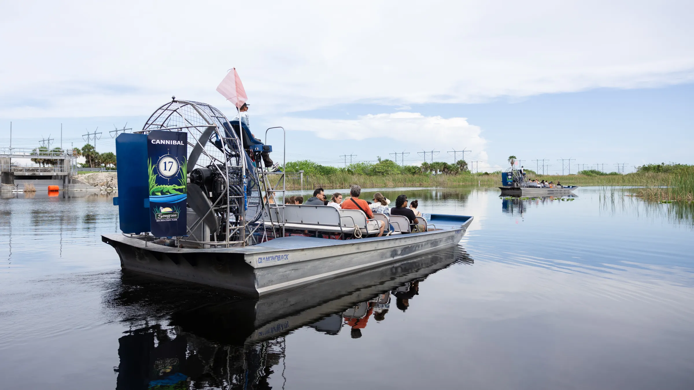 Airboat with passengers on a calm body of water under a cloudy sky.
