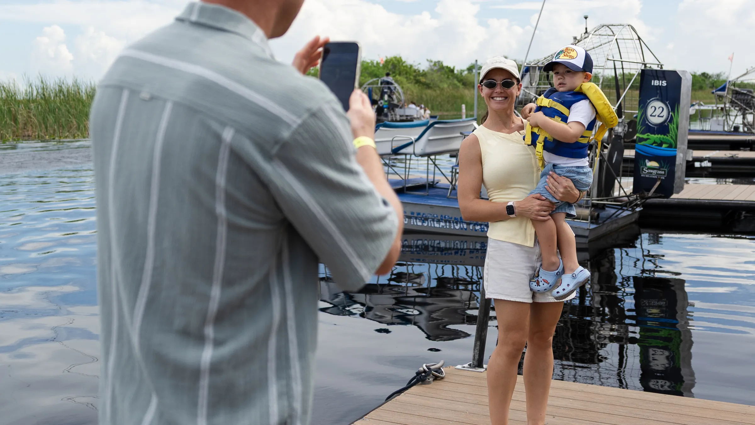 Man taking photo of woman holding child on a dock by a swamp boat.
