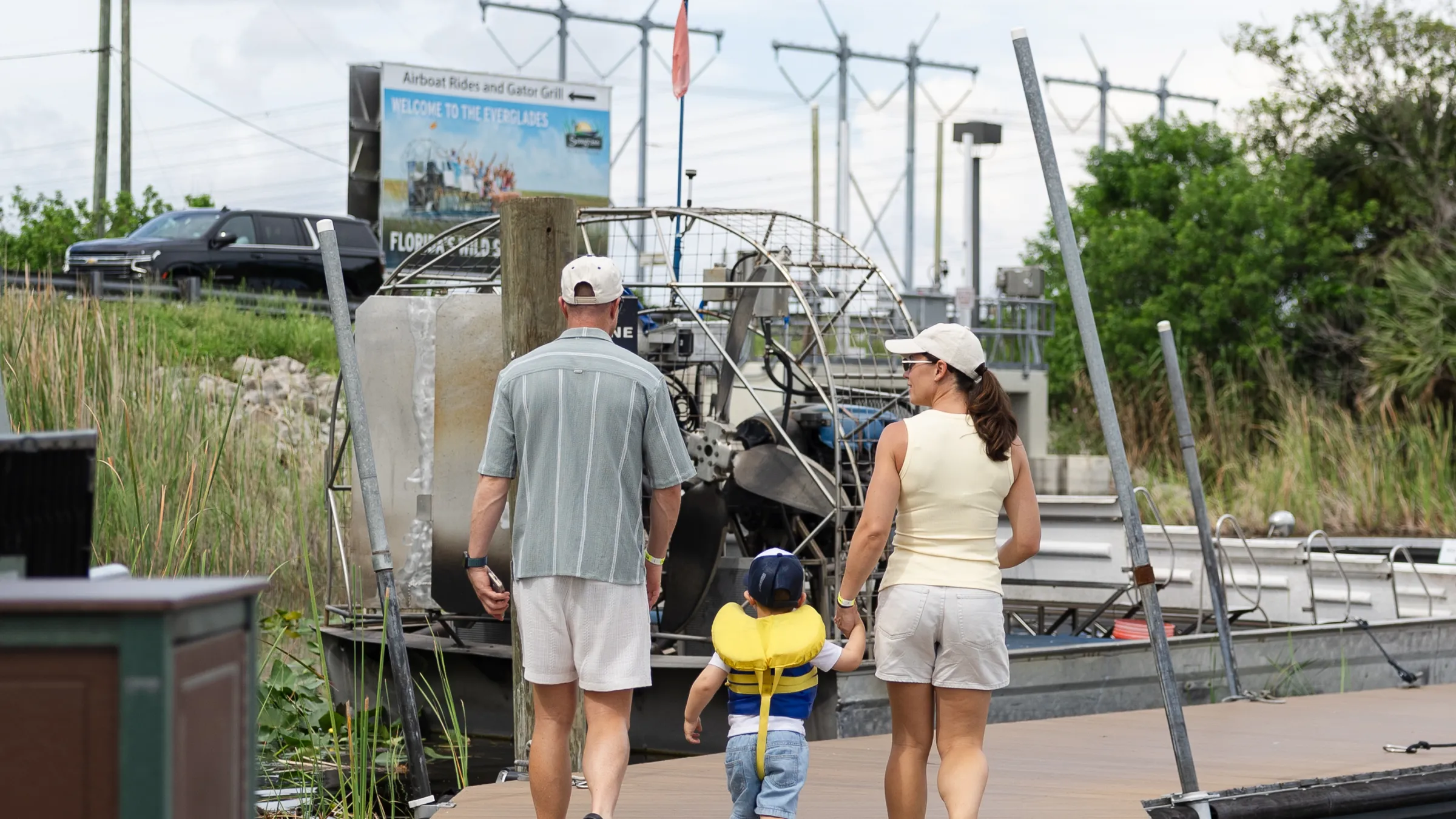 Family walking on a boardwalk near a boat dock.