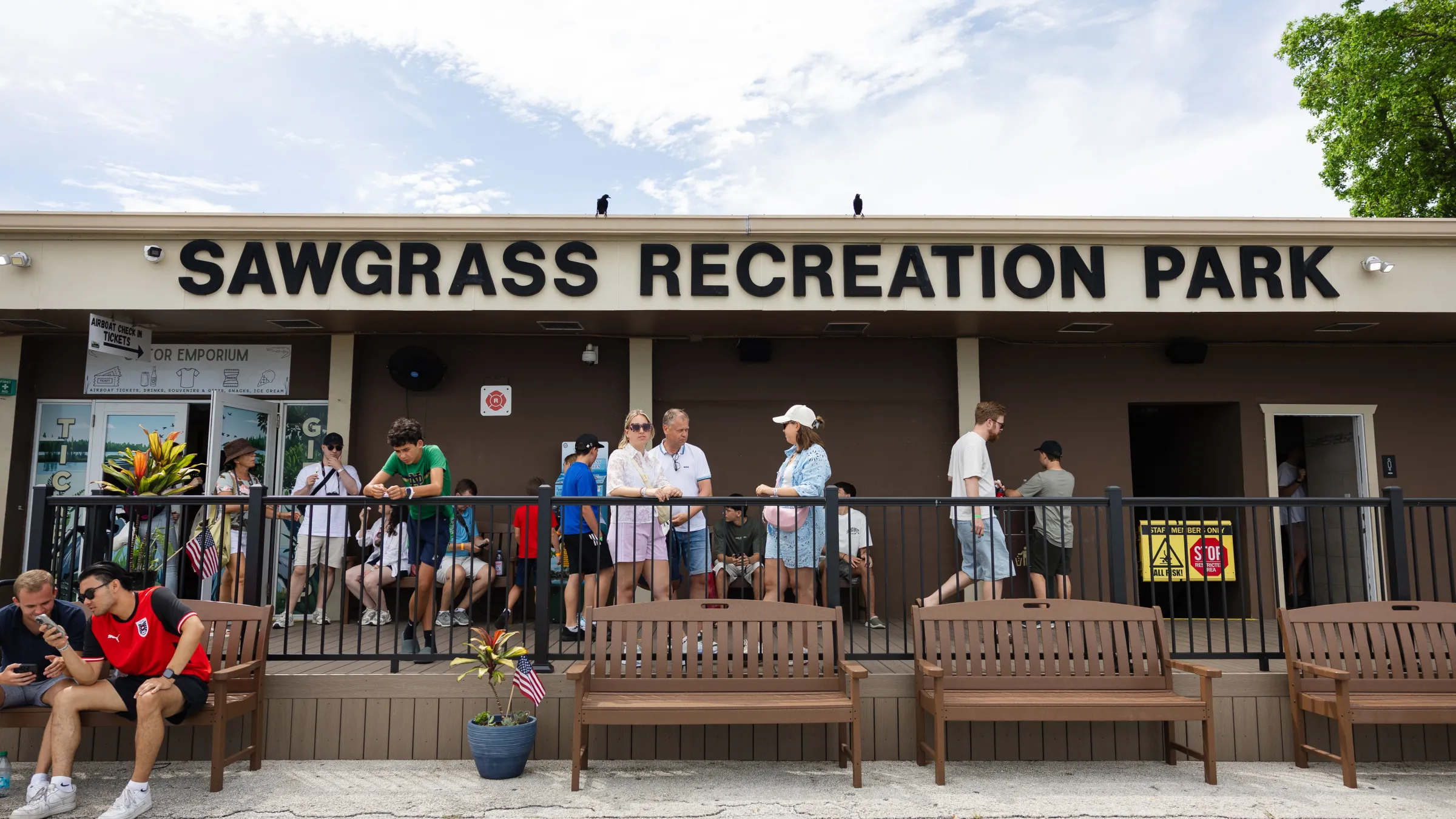 People outside Sawgrass Recreation Park building with benches and clear sky.