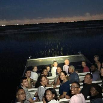 Group on airboat at dusk, with distant city lights on the horizon.