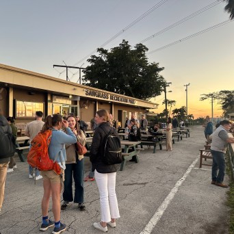 People gather outside a building labeled Sawgrass Recreation Park at sunset.