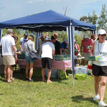 People gathered under a canopy, distributing items on a table outdoors.
