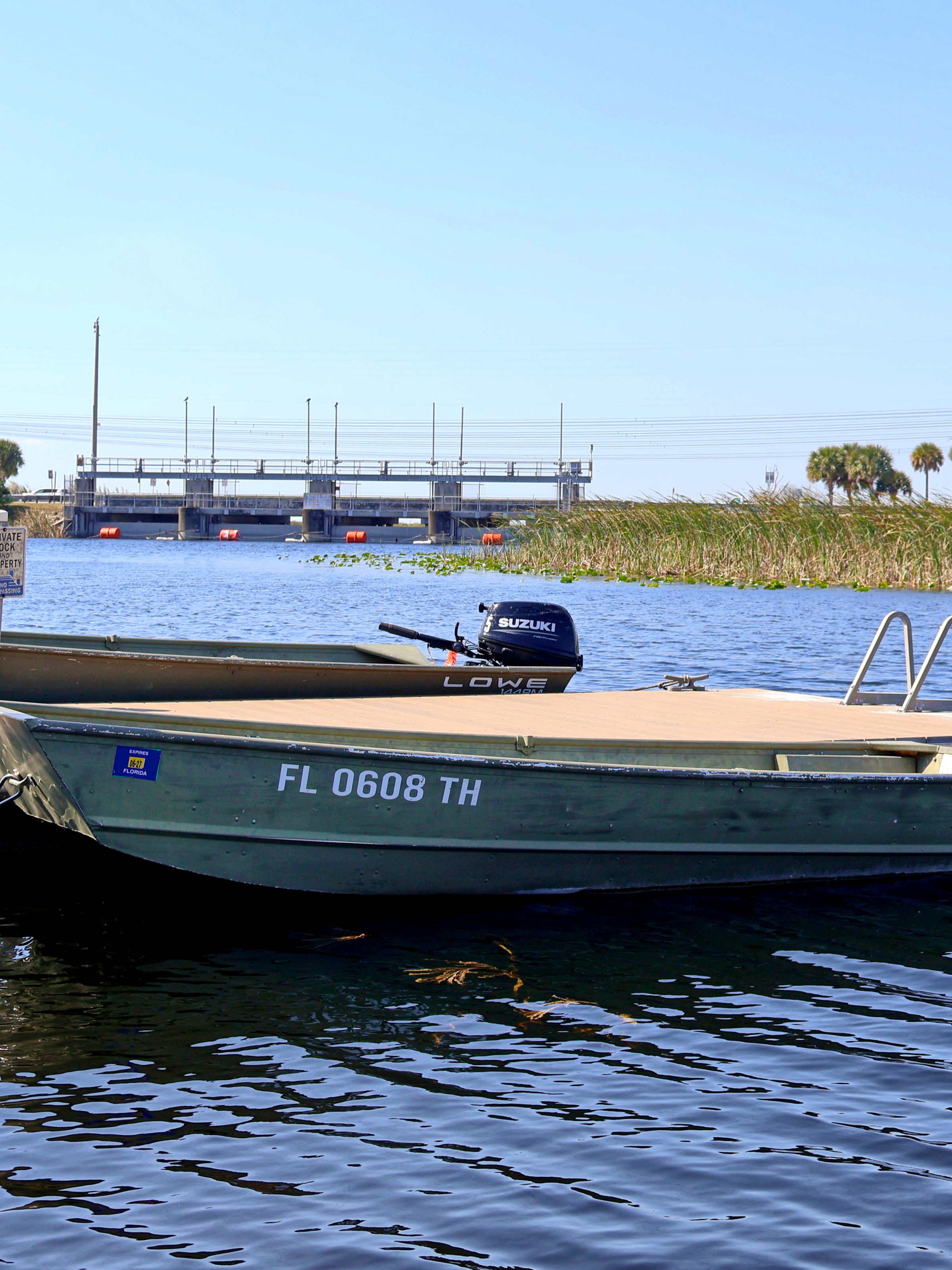 Two boats docked on a lake under a clear sky with trees and a structure in the background.