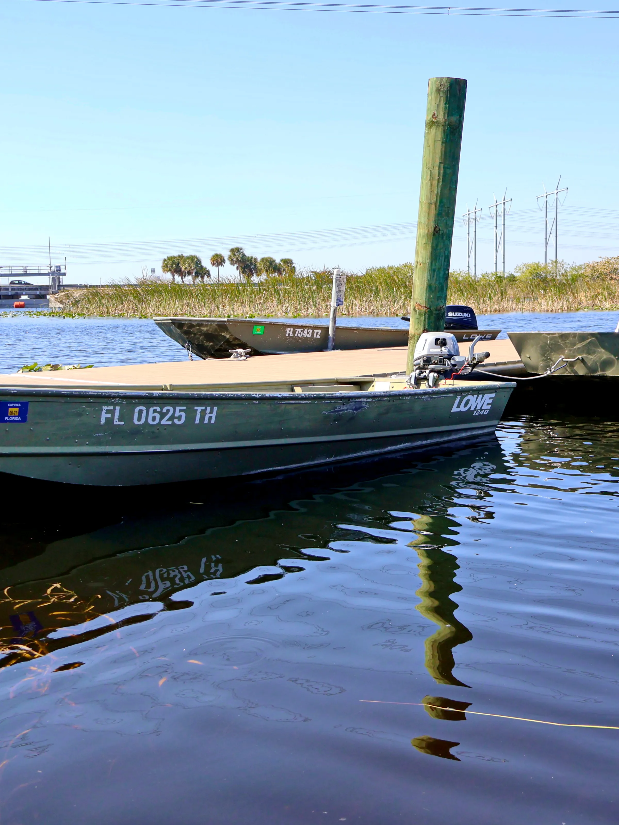 Two green motorboats docked on a calm lake with a bridge and trees in the background.