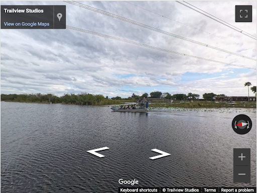 Airboat on a calm river under a cloudy sky, with distant trees and power lines visible.