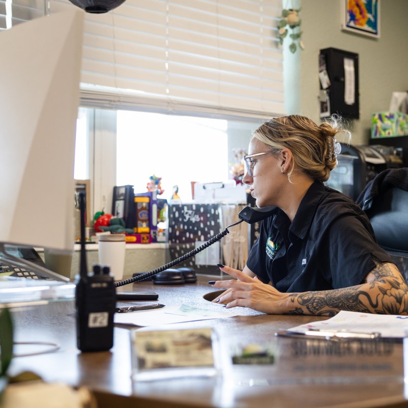 Woman with tattoos at a desk using a computer and phone in an office.