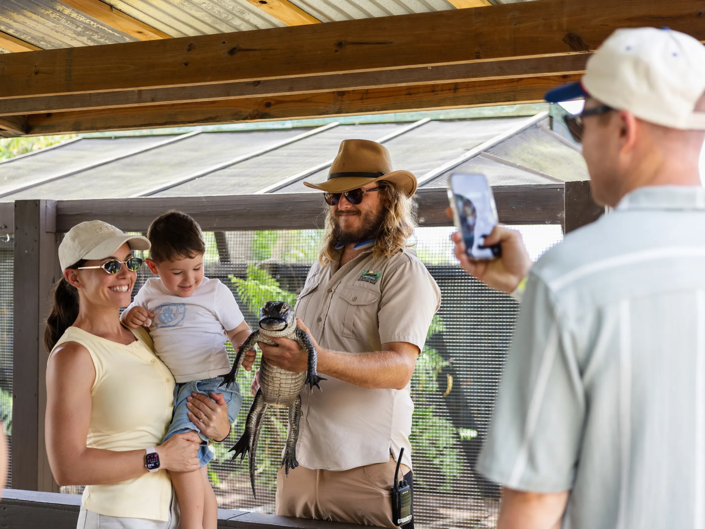 Family posing with a small alligator and zoo staff while being photographed.