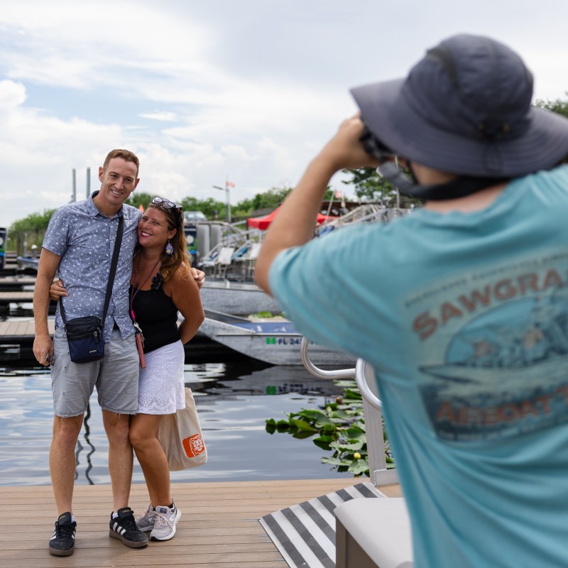 Three people at a dock; two pose, one photographs them.