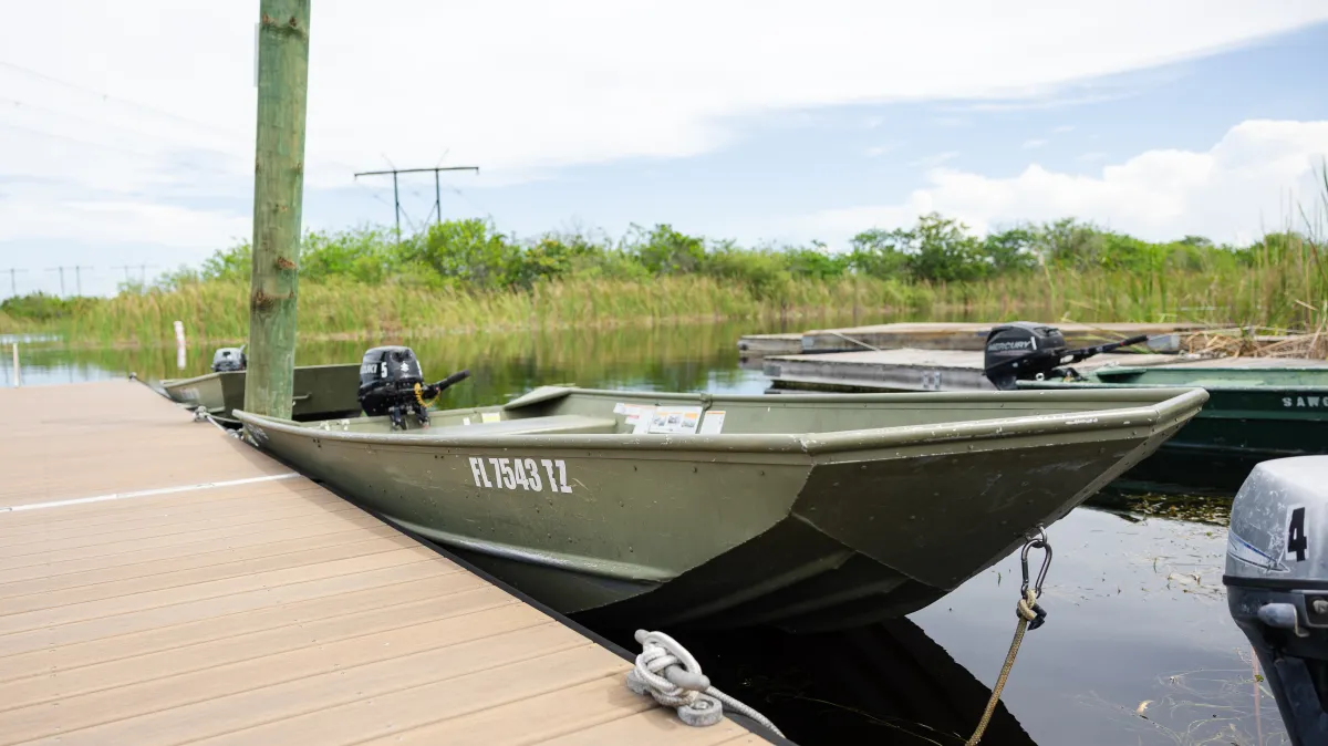 Green motorboat docked at a wooden pier on a calm lake.