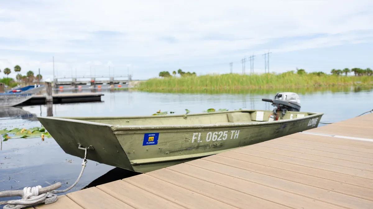 Small green boat docked on a wooden pier by a lake.